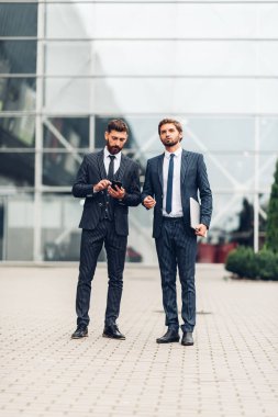 Modern bir şehirde strateji yi tartışan mavi takım elbiseli ve yürüyen iki iş adamı meslektaşı