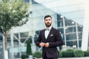 Genç ve başarılı. Takım elbiseli yakışıklı genç adam dışarıda dikilirken ceketini düzeltiyor.