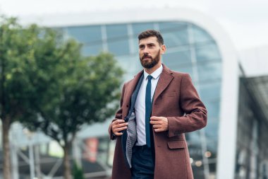 Sokakta yürüyen kahverengi ceketli genç bir adam. Kentsel arka planda modern saç stili ile genç adam.