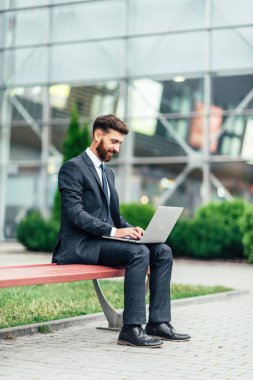 Mutlu, gülümseyen, şık adam modern ofis merkezi yakınında şehrin sokaklarında un üzerinde oturan ve onun laptop ile workin.