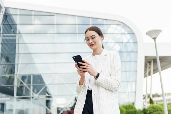 Ofis yakınında cep telefonu kullanarak Mutlu güzel esmer kız, güzel kadın telefon tarama ve alışveriş merkezi yakınında yürürken gülümseyerek bir mobil uygulama online alışveriş yapıyor.