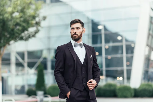 Genç ve başarılı. Takım elbiseli yakışıklı genç adam dışarıda dikilirken ceketini düzeltiyor.