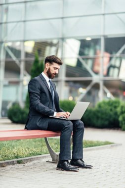 Mutlu, gülümseyen, şık adam modern ofis merkezi yakınında şehrin sokaklarında un üzerinde oturan ve onun laptop ile workin.