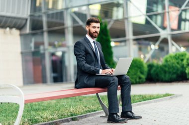 Mutlu, gülümseyen, şık adam modern ofis merkezi yakınında şehrin sokaklarında un üzerinde oturan ve onun laptop ile workin.