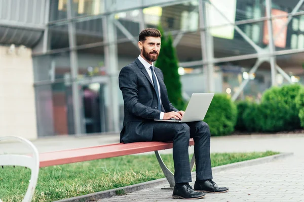Mutlu, gülümseyen, şık adam modern ofis merkezi yakınında şehrin sokaklarında un üzerinde oturan ve onun laptop ile workin.