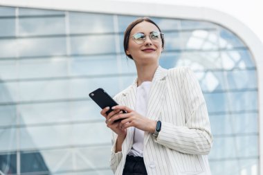 Beyaz gömlek giymiş ve şehrin dışında cep telefonu kısa mesaj yazarak profesyonel kadın işveren kopma yürürken modern akıllı telefon kullanarak güzel genç iş kadını