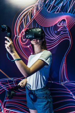 Oyun kulübünün karanlık odasında sanal gerçeklik kulaklık ve gamepads kullanarak oyun oynayan kadın