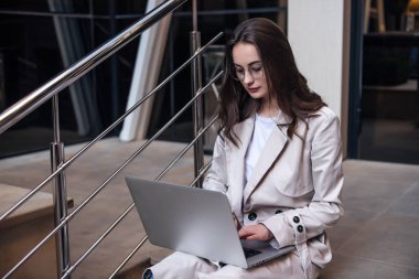 Modern iş merkezinde çalışırken bilgisayarını kullanan genç profesyonel iş kadınının yakın çekimi, arka planda modern binalar.