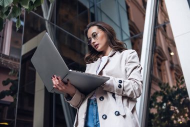 İş Parkı'nda oturma ve cep telefonuna metin yazarken onu laptop kullanarak meşgul satış kadın portresi. Çevrimiçi çalışıyorsanız işkadını.