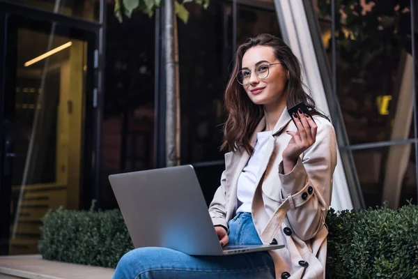 Kredi kartı tutan ve dizüstü bilgisayar kullanan genç bir kadın. Çevrimiçi alışveriş kavramı