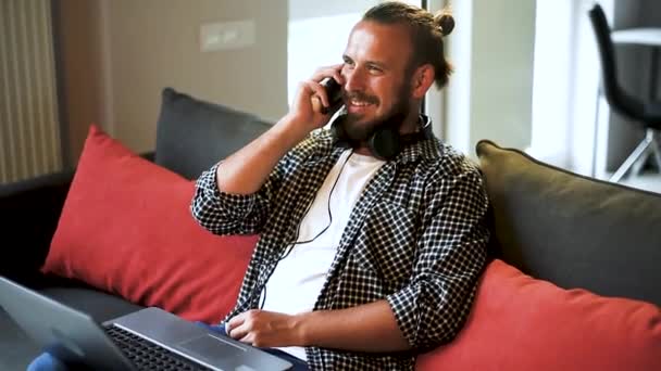 Bello giovane uomo che ride mentre prende una telefonata nel suo salotto. — Video Stock