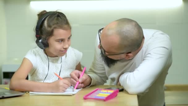 Young daughter gives dad a kiss as he helps girls with homework after school. — Stock Video