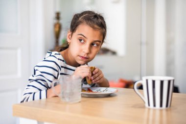 Evinde hamburger yiyen bir ilkokul öğrencisinin yakın görüntüsü. Kameraya bakıyor ve komik suratlar yapıyor..