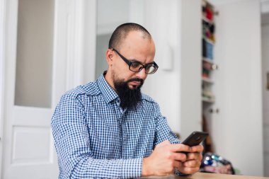 Oturma odasında oturan ve telefonu kullanan genç sakallı adam. Oturma odasında, sakallı, telefonla konuşan delikanlıyı yakından çek. Portre. Kapalı.