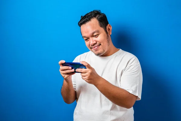 Funny Fat Asian Guy Playing Games on Tablet Smart Phone against blue background