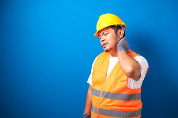 An asian fat worker wearing safety helmet feeling pain on his neck against blue background