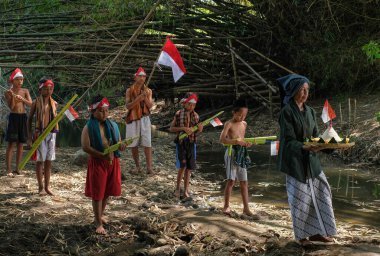 Yogyakarta - 23 Ağustos 2020: Geleneksel giysiler giyen ve pirinç taşıyan bir büyükanne, Endonezya 'nın bağımsızlık gününü anmak için bayrak taşıyan küçük bir çocuk tarafından eşlik ediliyor.