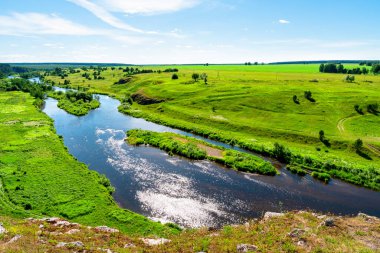 Uçurumun tepesinden nehrin ortasına kadar olan ada manzarası. Mavi gökyüzü nehrin suyuna yansıyor. Dağlık çayırlı tepeler