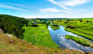 Nehir ve ormanın üzerinde yaz günbatımı. Uçurumdan nehre kadar güzel bir manzara ve yeşil çimlerle dolu bir sahil.