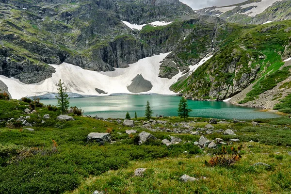 높은 산에 있는 아름다운 청록색 호수. 산 비탈에 있는 빙하가 호수에 물을 공급하고 있습니다. 전경에는 커다란 돌들이 있고 산으로 둘러싸인 호수가 있는 산 풍경. — 스톡 사진