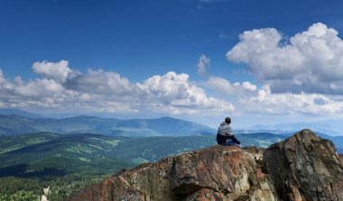 Bir adam bir uçurumun kenarına oturur ve dağlara doğru bakar. Altai Rusya