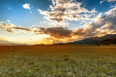 Altai 'deki Kurai bozkırında gün batımı, güneş ışınları bulutların arasından geçer. Rusya