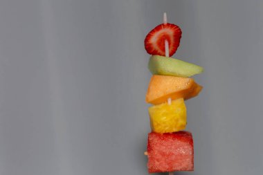 Plastik bir şiş sulu meyve parçaları kesmiştir: çilek, ballı kavun, kavun, ananas ve karpuz ve beyaz bir arkaplan önünde bekletilir..