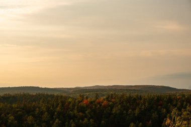 Akşam ışığında, sonbahar renklerine sahip ormanlık tepeler bulutlu, puslu gökyüzü manzaralı, sakin bir manzarada görülür..