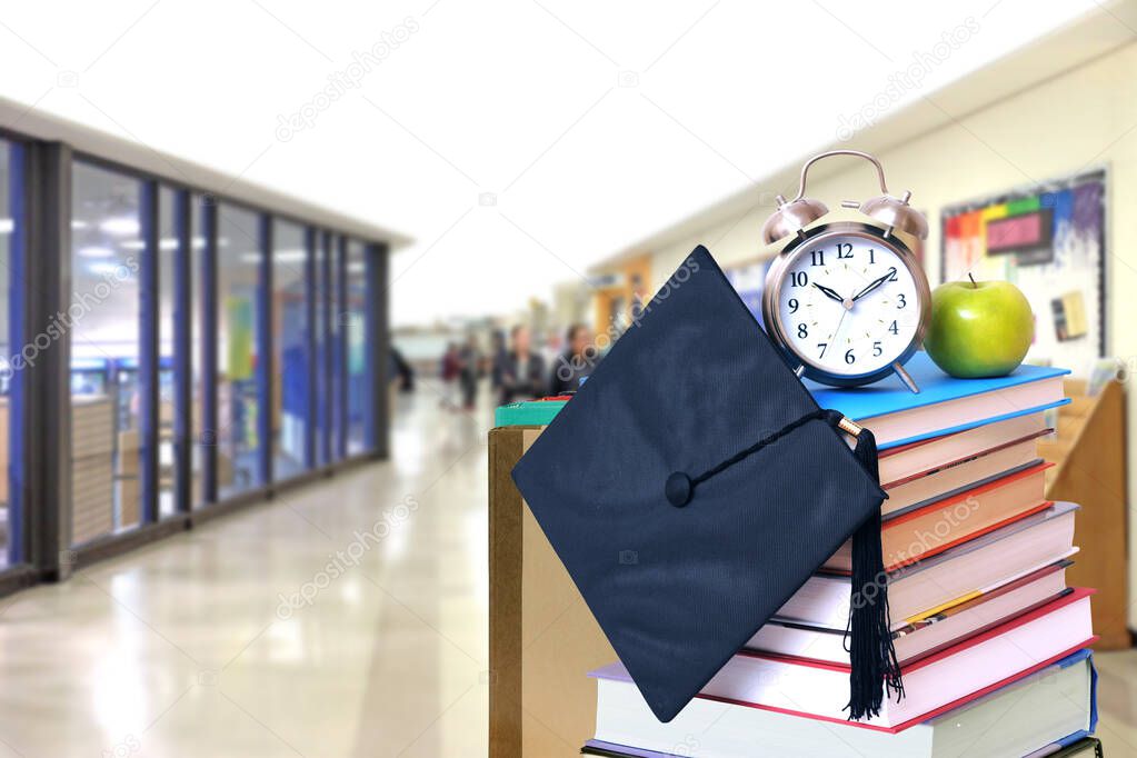 Closeup of pile of books with alarm clock on blurred school hall background, education concept 