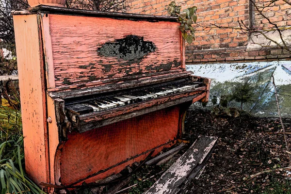 Old broken red piano with peeled paint from rain and wind, outside on an autumn day. Discarded unnecessary musical instrument.