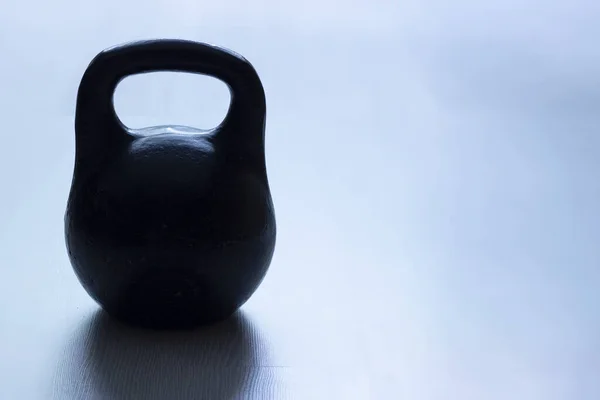 Old sports weightlifting equipment - cast iron kettlebell on a blue background with copy space.