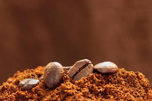 Roasted grains of arabica coffee on ground coffee close-up on a brown background.