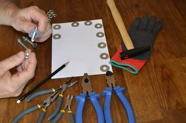 A man works with a bench tool and takes notes on a white sheet.