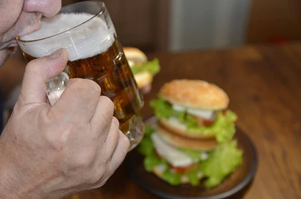 A man drinks beer and eats a delicious burger.