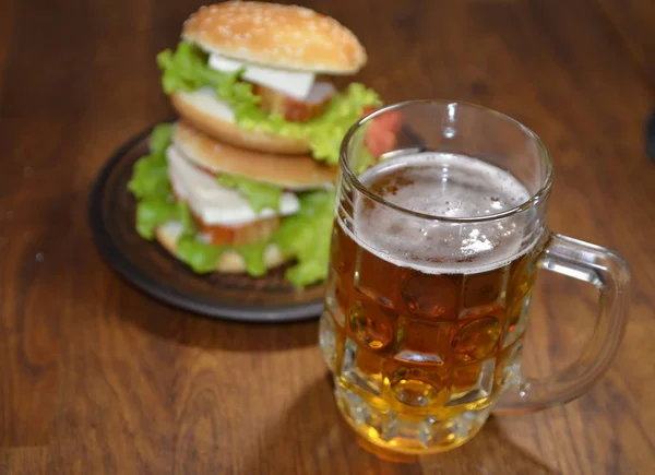 On the table is a glass of beer and a delicious burger.