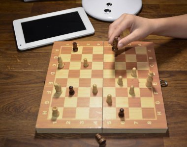 Masanın üzerinde bir tablet, bir satranç tahtası ve figürleri yeniden düzenleyen bir çocuk eli var..