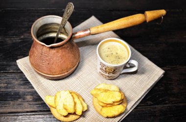 Masanın üzerinde yeni demlenmiş kahve, bir fincan kraker ve bakır çubuk var..