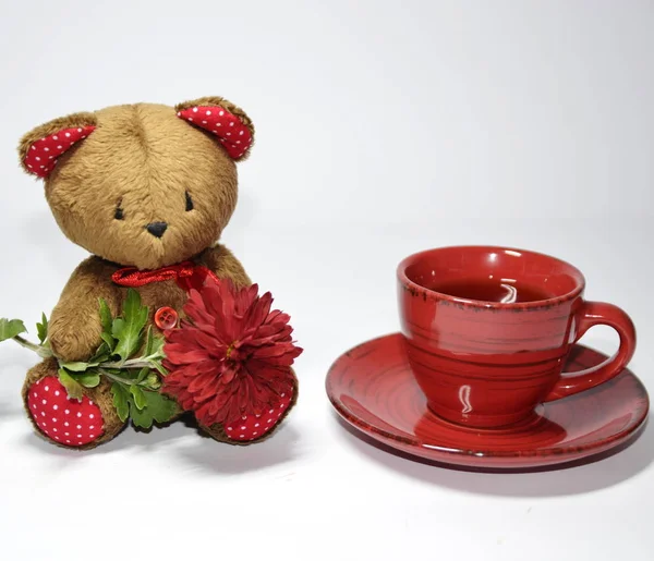 On the table is a cup of tea and a cute teddy bear with a flower.