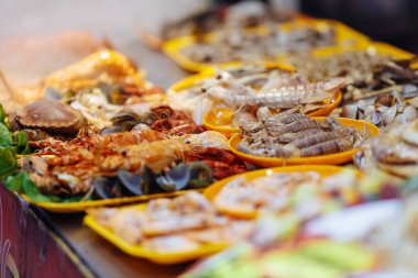 Egzotik bir ülkede hafta sonu gece pazarında plastik tabaklar üzerinde çeşitli taze deniz ürünleri. Turistler için lezzetli renkli Asya yemeği. Bulanık arkaplan