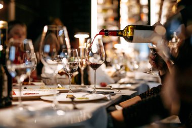 Lüks restoranlarda kırmızı şarap tatma işini kapayın. Aklı başında insanlar ve enfes içecekler için yapılmış. Parlak kadehler, tabaklar ve tabaklar bulanık arka planda..