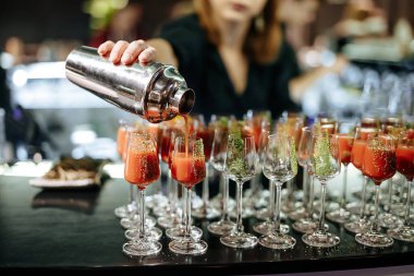 Kadın barmenin, alkollü kokteyller yapmak ve aynı bardaklara doldurmak için profesyonel karıştırıcı kullanmasına yakın çekim. Parti ve tost kavramı