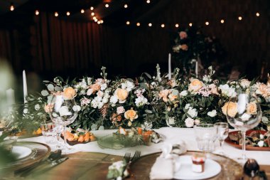 Kutlama masasında tabaklar, çatal bıçak takımı ve lezzetli yemekler var. Çiçek kompozisyonu ve mumlar dekorasyon için yapıldı. Renklerin şık kombinasyonu.