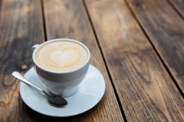 Tahta masada servis edilen beyaz seramik bardakta güzel latte sanatıyla taze, lezzetli bir kahve. Sıcak sabah içeceği ve yaşam tarzı kavramı.