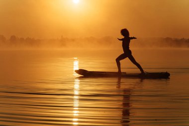 Yemek masasında dururken yoga egzersizleri yapan güçlü genç adam. Silüetteki aktif adam dışarıda antrenman yaparken sabah güneşinin tadını çıkarıyor..