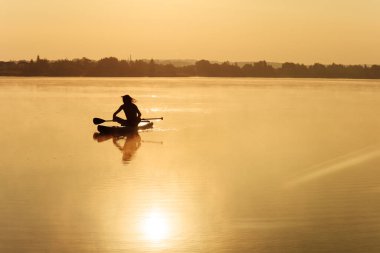 Gölde sup sörfü yapan atletik erkek silueti. Doğada aktif eğlence kavramı. Arka planda inanılmaz yaz günbatımı.