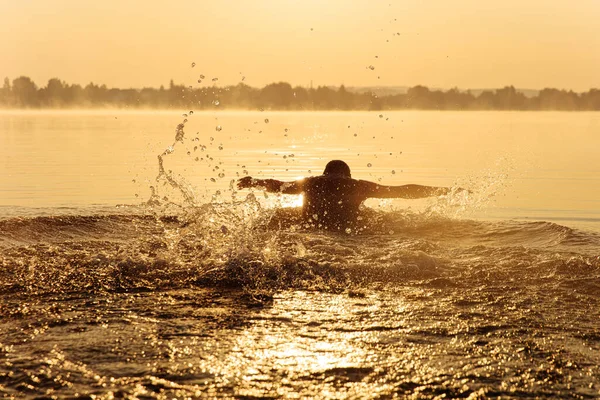 瘦小的年轻人在湖面上积极地游泳 并在水面上洒水 强壮有力的男子在早晨利用新鲜空气进行锻炼的轮廓 — 图库照片