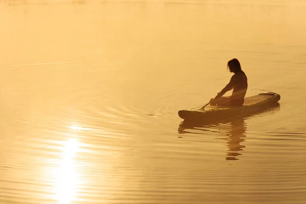 在雾蒙蒙的湖心区 年轻的划桨者穿着人物造型在浅水板上放松 快乐的运动员在大自然的锻炼中享受美丽的日出 — 图库照片