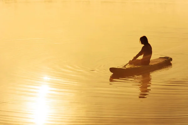 Jovem macho paddler em silhueta relaxante na prancha de jantar — Fotografia de Stock