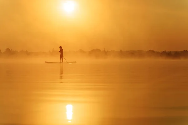 Jovem usando prancha de remo para nadar no lago — Fotografia de Stock