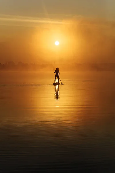 Jovem praticando em sup surf durante o nascer do sol incrível — Fotografia de Stock
